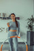 Das Bild zeigt eine lächelnde Frau in einem grauen Sport-Outfit, die einen Hula-Hoop-Reifen hält und eine Flasche Live Fresh Saft in der Hand hat. Die Szene wirkt freundlich und motivierend, mit einem Fokus auf Fitness und Gesundheit.