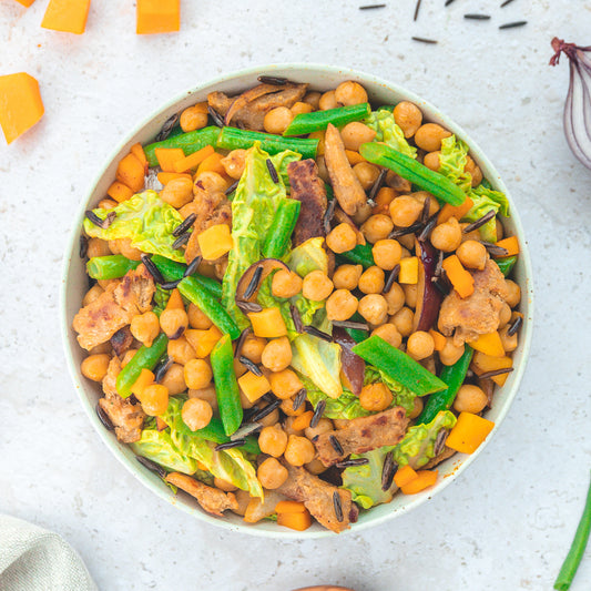 Eine bunte Bowl, gefüllt mit Kichererbsen, grünen Bohnen, Wildreis, Kürbiswürfeln, Salat und Fleischersatzstreifen. Die farbenfrohe Mischung suggeriert eine gesunde, vegane Mahlzeit mit viel Gemüse und pflanzlichen Proteinen.