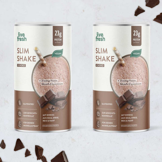 Zwei Dosen Live Fresh Slim Shake Schoko mit der Aufschrift 23 g Protein pro Portion und vegan vor hellem Hintergrund mit Schokoladenstücken dekoriert. Auf der Verpackung stehen Hinweise wie glutenfrei zur Gewichtskontrolle und mit Eiweiß aus Soja Erbse Reis und Hanf.
