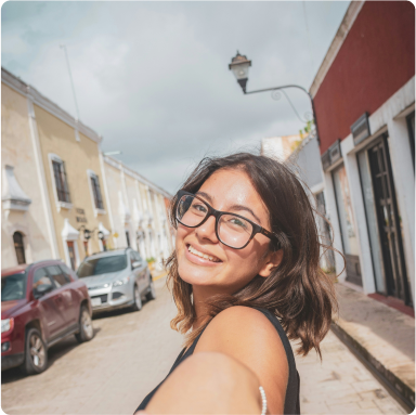 Lächelnde brünette Frau mit schwarzer Brille, die auf der Straße ein Selfie von sich macht.