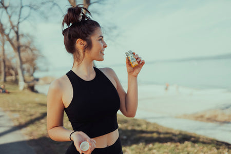 Frau im Sportoutfit hält einen Kurkuma-Shot von LiveFresh in der Hand, während sie draußen trainiert