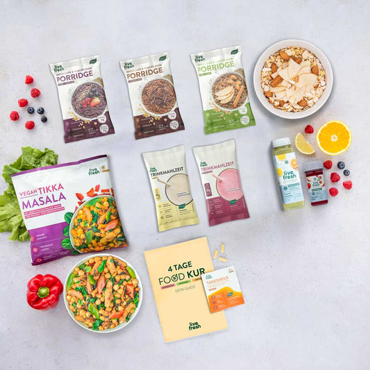 Übersicht der „4 Tage Food Kur“ von LiveFresh: Enthalten sind drei Sorten Porridge, zwei Trinkmahlzeiten, zwei kleine Shots, ein veganer Tikka-Masala-Bowl, frisches Obst und Gemüse sowie ein Guide mit Nahrungsergänzungsmitteln. Die Produkte sind ansprechend auf einem hellen Untergrund arrangiert.