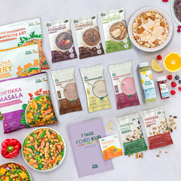 Zeigt eine Auswahl an Produkten für eine 7-Tage-Food-Kur von „Live Fresh“. Es enthält verschiedene Porridge-Sorten, Trinkmahlzeiten, vegane Mahlzeiten wie Tikka Masala und Kichererbsencurry, sowie Protein-Snacks und Getränke wie Säfte und Nahrungsergänzungsmittel. In der Mitte befindet sich ein lila Heft mit der Aufschrift „7 Tage Food Kur – Dein Guide“ und eine Packung „Tagesheld“-Kapseln. Frische Früchte wie Beeren und Orangenscheiben dekorieren die Szene.