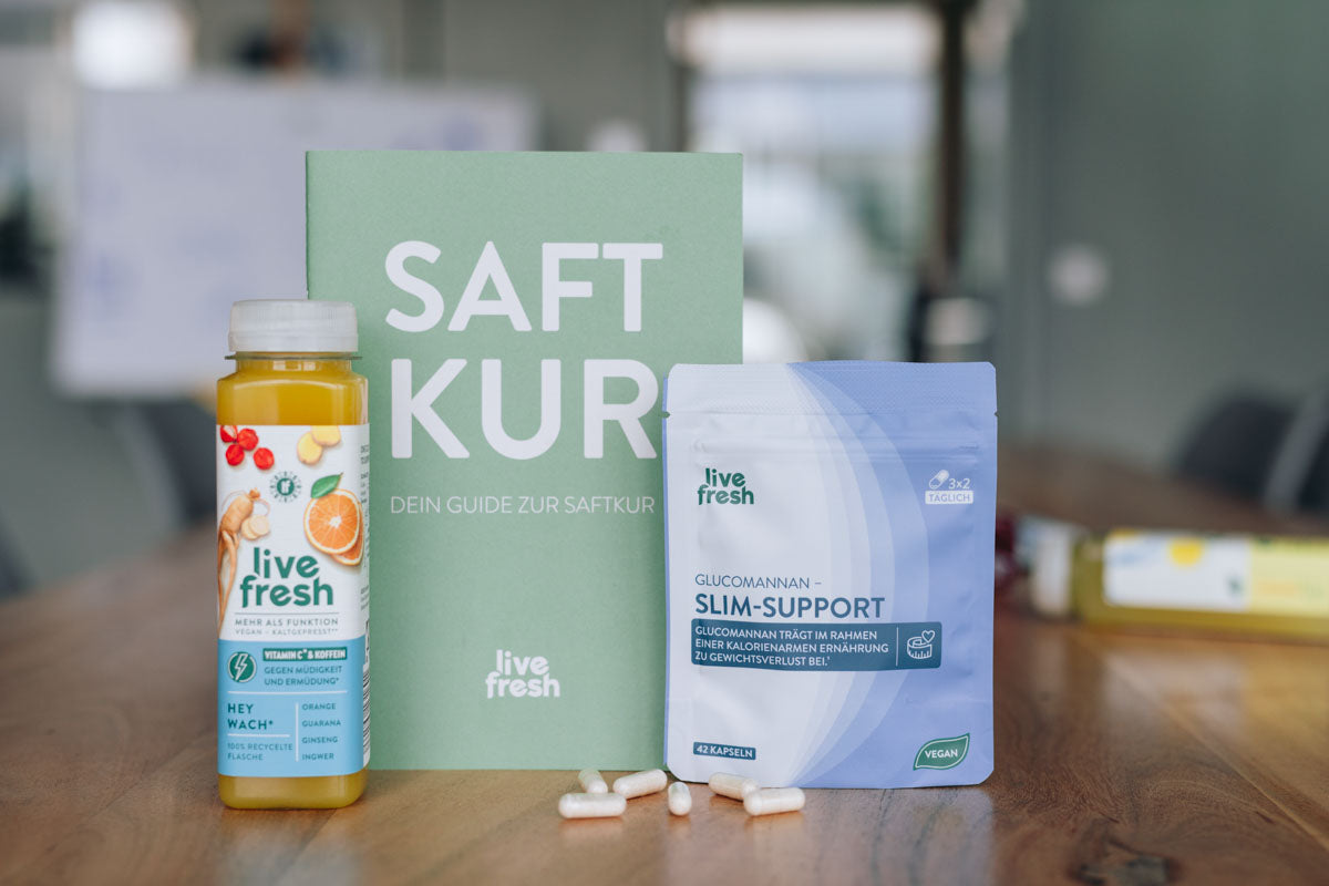 Hey Wach Saft, Saftkur Guide & Glucomannan Slim Support von LiveFresh angerichtet auf einem Tisch mit weiteren Flaschen der Saftkur im Hitnergrund, sowie Slim-Support Kapseln auf dem Tisch. 