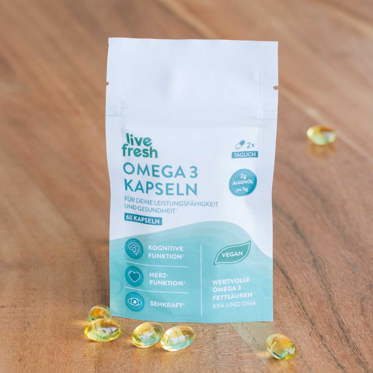 Omega-3-Kapseln von LiveFresh Sowohl die Verpackung als auch die Kapseln vor hölzernem Hintergrund. Auf der Verpackung steht täglich 2x, 60 Kapseln und für deine Leistungsfähigkeit und Gesundheit. 