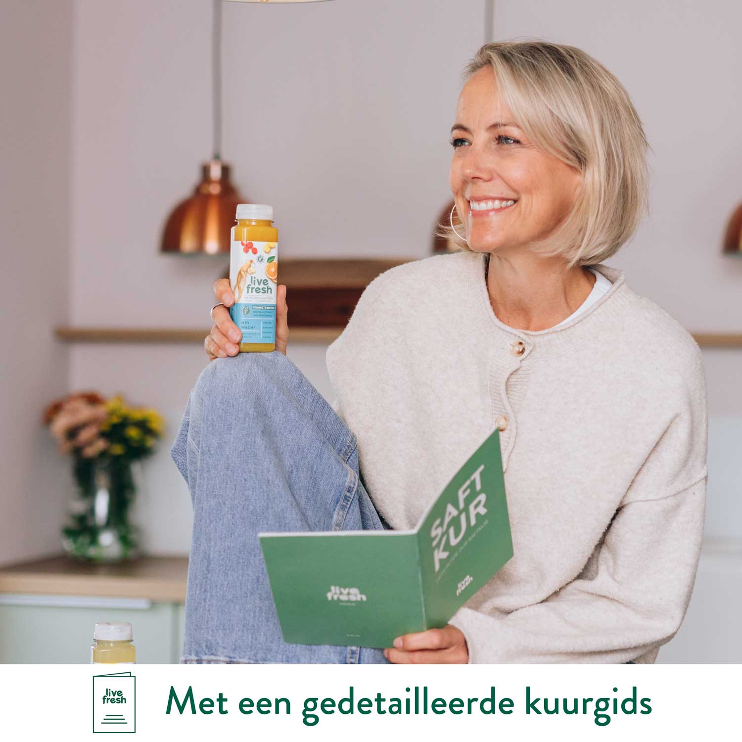 Glimlachende vrouw houdt een LiveFresh sapfles vast terwijl ze een kuurgids leest in een gezellige keuken.