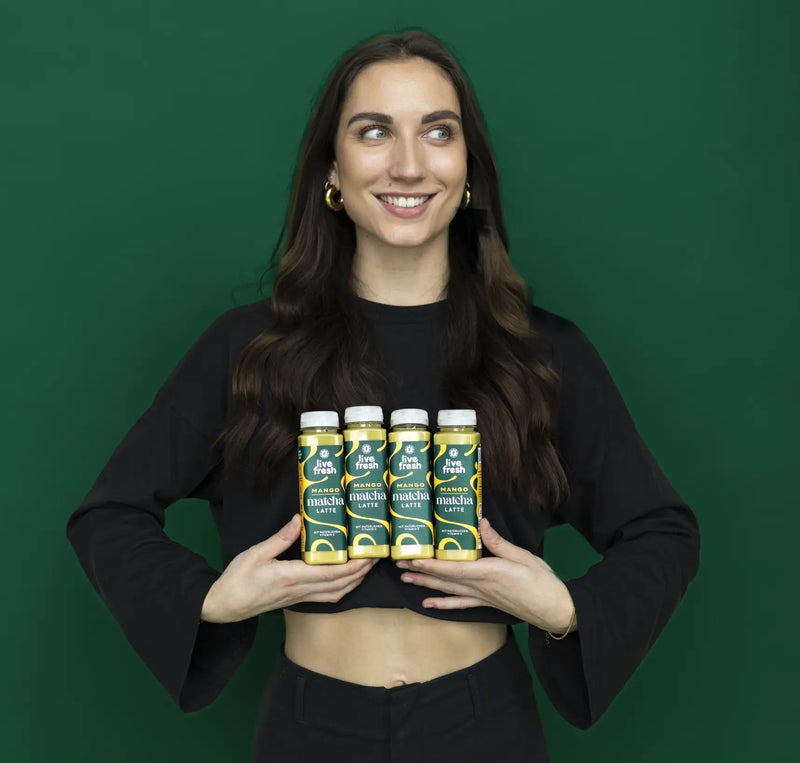 Person smiling while presenting LiveFresh mango matcha latte in a small bottled drink. The product is centered and easy to identify.