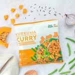 LiveFresh "Kurkuma Curry" Tiefkühlgericht in der orangenen Verpackung, umgeben von frischen Zutaten wie Kürbisscheibe und Kürbiswürfeln, grünen Bohnen, roter Zwiebel und Wildreis auf einer hellen Oberfläche. Ein Holzlöffel und ein Küchentuch liegen daneben.